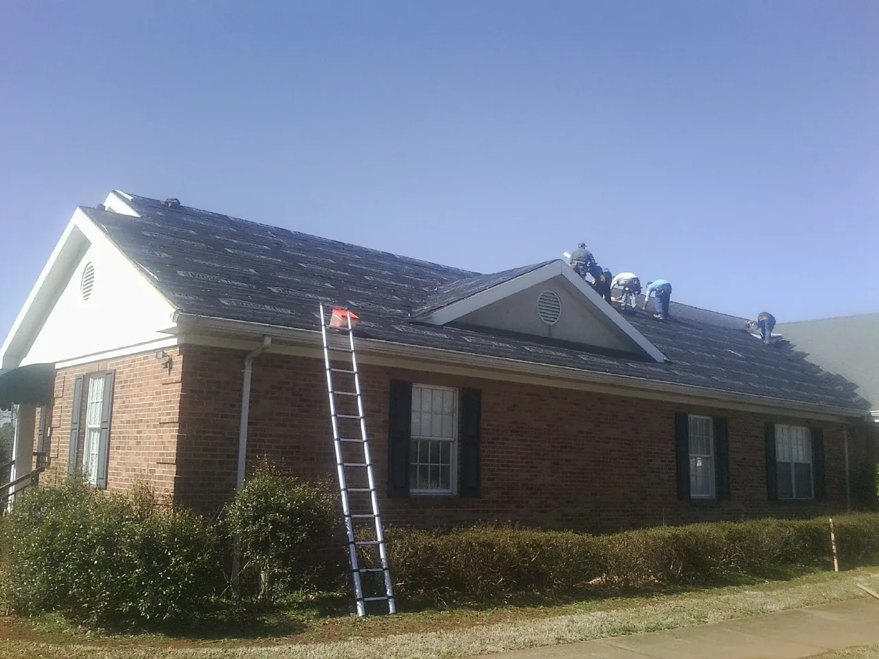 Crew tearing shingles off a brick ranch roof with a ladder set — Metal Roof Repair work by our crew in Laurel Bloomery