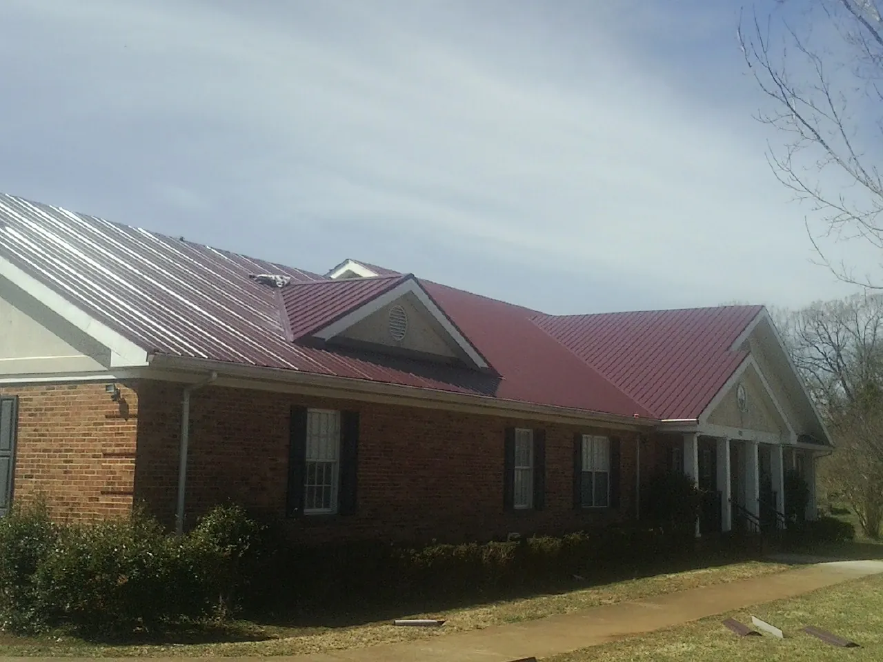 Red metal roof with gabled entries on a long brick building, from a Hail Damage Roof Repair job in Laurel Bloomery