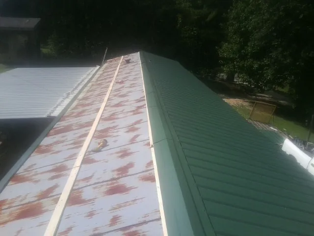 Old rusted panels beside newly installed green metal roofing — Wind Damage Roof Repair by Roofing Brothers in Laurel Bloomery