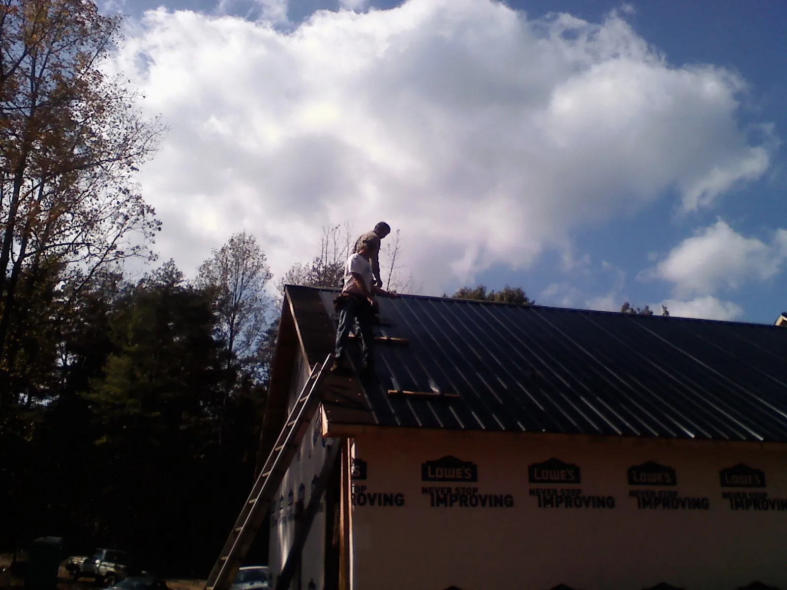 Roofer fastening dark metal panels high against a cloudy sky, from a Roof Inspection job in Laurel Bloomery