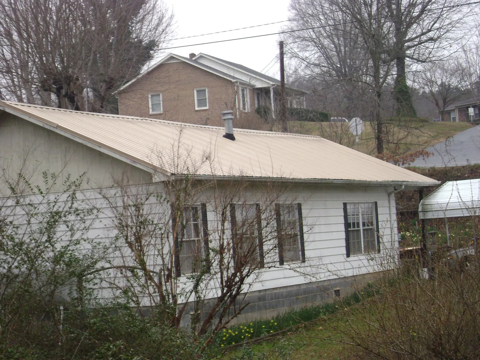 Tan metal roof on a white sided house set into a hillside — Commercial Roofing by Roofing Brothers in Laurel Bloomery